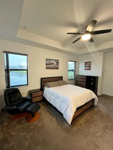 Tray ceiling with central light fixture, wall-to-wall carpeting, and dual windows