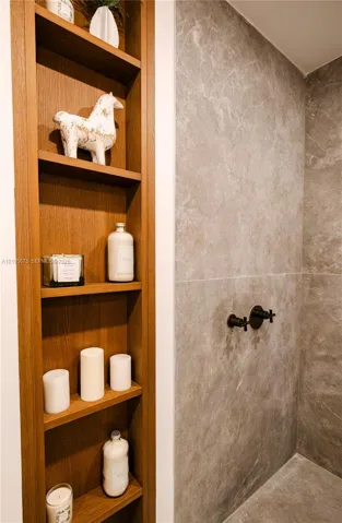 Built-in recessed wood shelving featuring multiple tiers, complemented by large-format stone-finish wall tile and matte black wall-mounted faucet fixtures. Images are for finish purposes only. Please refer to the floor plan for the layout.
