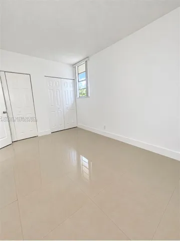 Interior space featuring neutral large-format tile flooring, white walls, two sets of white panel doors with brushed metal hardware, and a single vertical window