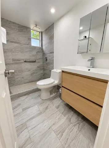 Modern bathroom featuring a wood-finish floating vanity, walk-in shower with floor-to-ceiling tile, rectangular integrated sink, and mirrored medicine cabinet