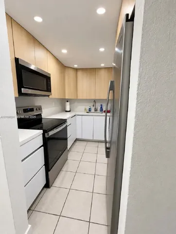 Kitchen featuring two-tone cabinetry, white countertops, stainless steel appliances, and tile flooring