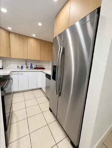 Kitchen featuring stainless steel appliances, white quartz countertops, light wood-finish cabinetry, and ceramic tile flooring