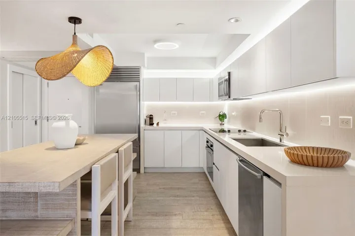 Contemporary kitchen featuring flat-panel white cabinetry, stone-surface countertops, under-cabinet lighting, stainless steel appliances, and wood-finish flooring