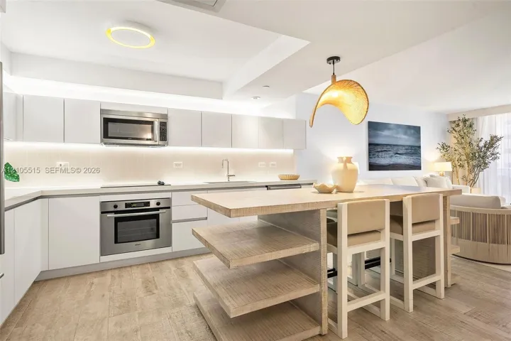 Kitchen featuring white flat-panel cabinetry, stainless steel appliances, under-cabinet lighting, wood-finish flooring, and a central island with built-in shelving