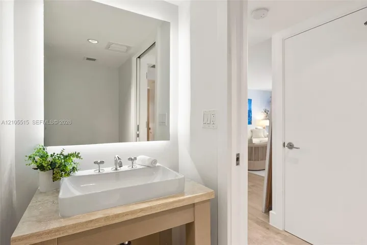 Floating vanity featuring a stone countertop, rectangular vessel sink, polished chrome widespread faucet, and a large backlit wall-mounted mirror