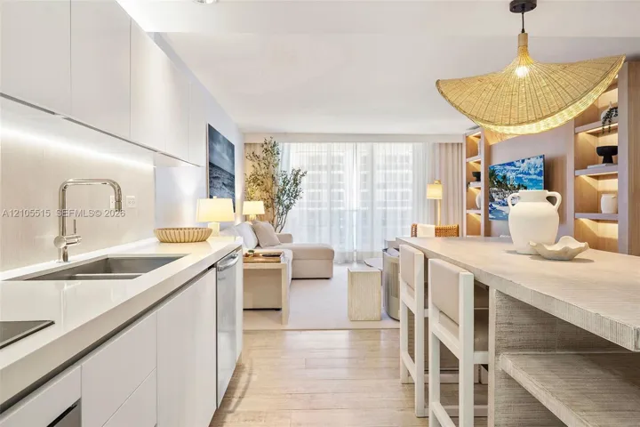 Contemporary kitchen featuring white flat-panel cabinetry, light-toned stone countertops, integrated under-cabinet lighting, wood-finish flooring, and built-in floor-to-ceiling shelving