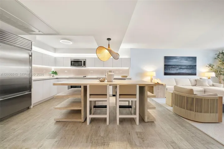 Kitchen featuring wood-finish flooring, white flat-panel cabinetry, stainless steel refrigerator, recessed lighting, and a kitchen island with built-in shelving
