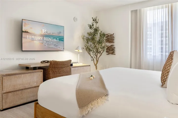 Neutral-toned room featuring a large floor-to-ceiling window dressed with sheer curtains and light wood-finish flooring