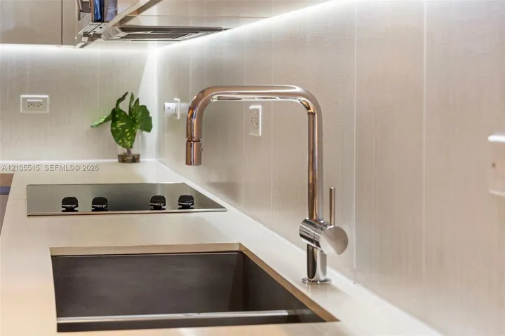 Polished chrome high-arc kitchen faucet, undermount sink, solid surface countertop, smooth-finish wall paneling, and integrated under-cabinet lighting