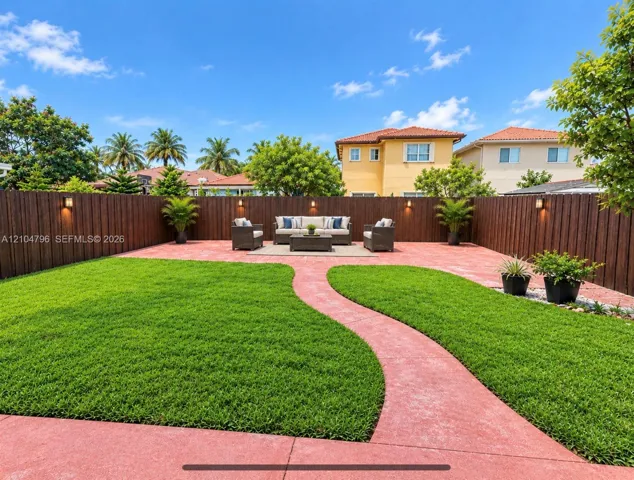 Backyard featuring a concrete paver patio, manicured lawn, full-height privacy fencing, and wall-mounted exterior lighting