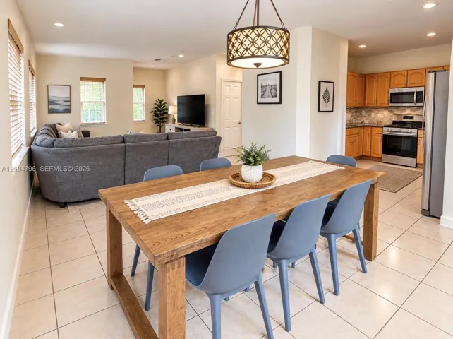 Open-concept interior featuring large-format tile flooring, recessed lighting, a decorative drum pendant fixture, and a kitchen equipped with natural wood cabinetry and stainless steel appliances