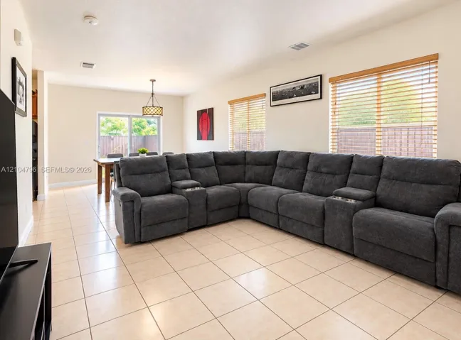 Open-concept interior featuring large-format ceramic tile flooring, multiple windows with horizontal blinds, and a hanging drum pendant light fixture