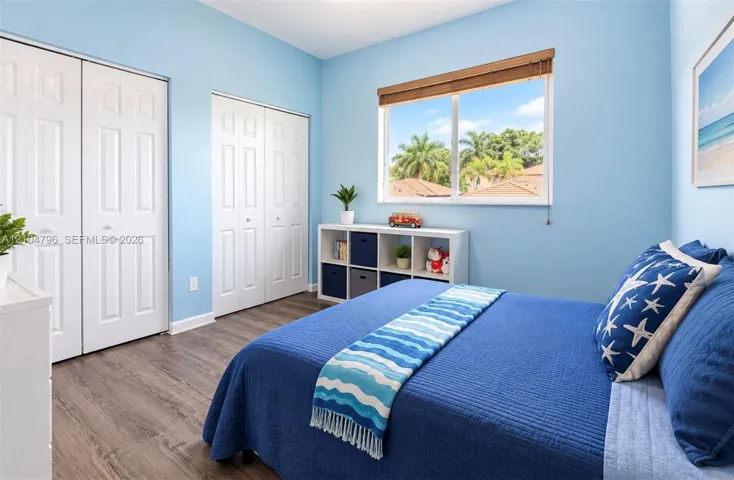 Room featuring wood-finish flooring, dual-door closets, and a window with wood-slat blinds