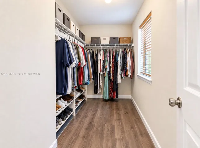 Walk-in closet featuring wood-finish flooring, built-in wire shelving, and a window with blinds