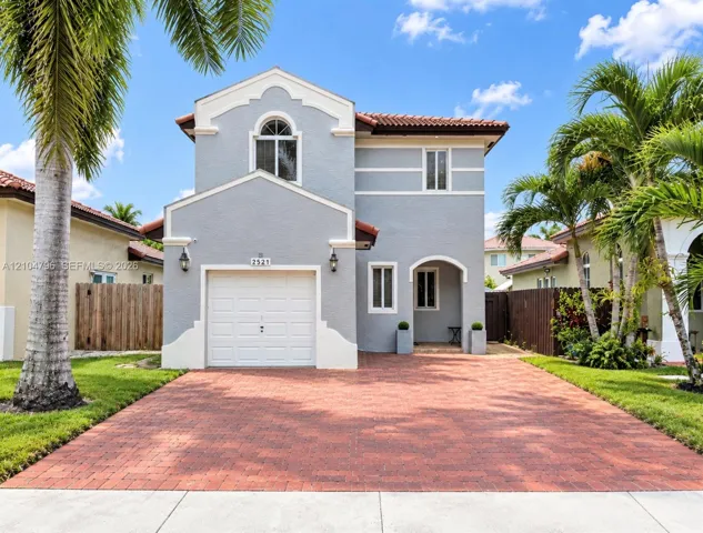Two-story residence featuring a textured stucco exterior, decorative white trim, red tile roofing, an arched entryway, and a paved brick driveway