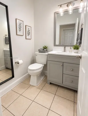 Bathroom featuring a grey vanity with satin-finish hardware, a crisp white countertop with an integrated sink, ceramic tile flooring, and a framed mirror with three-light fixture