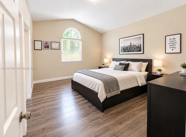 Room featuring vaulted ceilings, wood-finish flooring, and an arched window