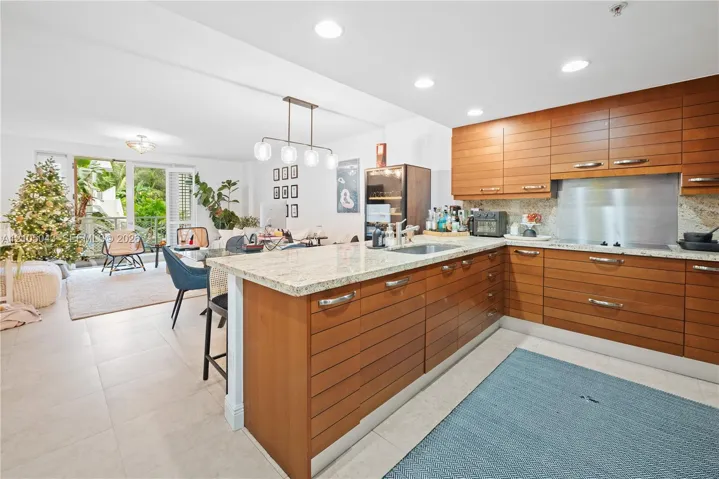 Kitchen featuring horizontal-slatted cabinetry, light-toned stone countertops, a metallic backsplash, recessed lighting, and tile flooring