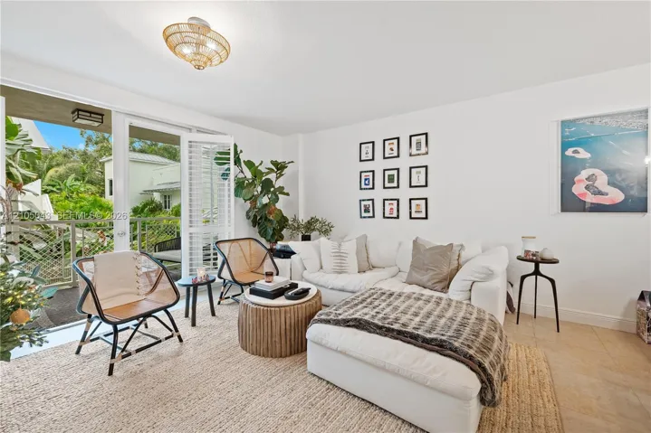 Living area featuring neutral tile flooring, a woven semi-flush mount light fixture, and floor-to-ceiling glass doors opening to a covered balcony with metal railing