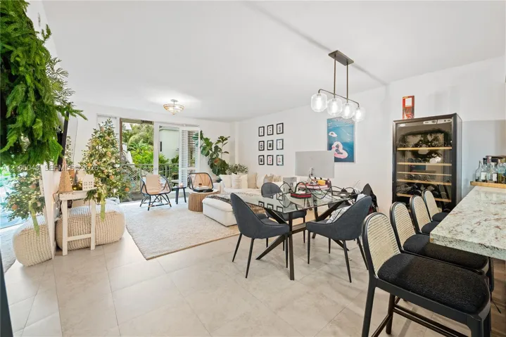 Open-concept interior featuring large-format tile flooring, stone countertop with integrated breakfast bar, built-in wine refrigeration unit, modern multi-light pendant fixture, and sliding glass doors