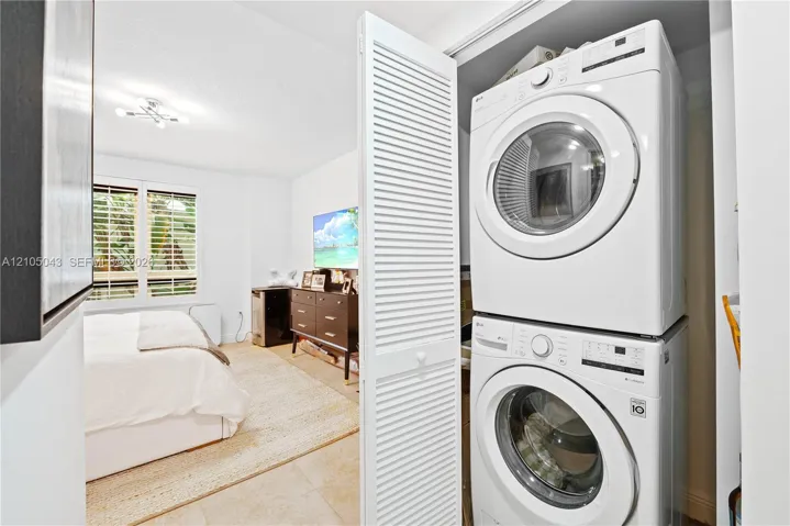 Stackable laundry unit housed within a closet featuring white louvered doors