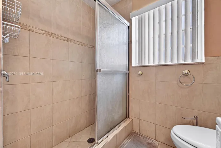 Tiled shower enclosure with a glass sliding door, neutral wall tile, and vertical window blinds