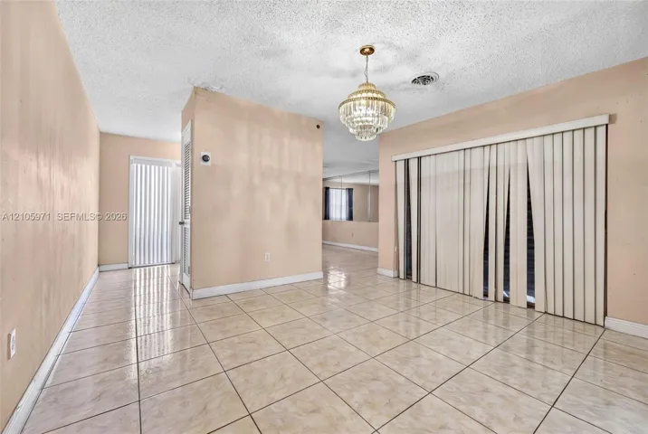 Ceramic tile flooring, tiered crystal chandelier, sliding glass door with vertical blinds, and wall-mounted mirror paneling