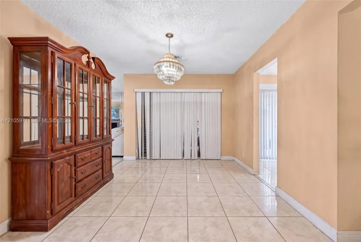 Large-format neutral tile flooring throughout, multi-tiered crystal pendant light fixture, and floor-to-ceiling vertical window blinds