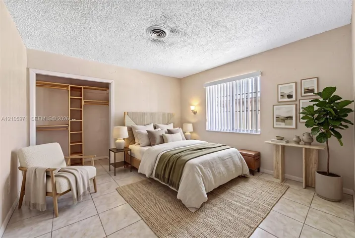 Neutral-toned interior featuring tile flooring, textured ceiling, built-in closet shelving, and vertical window blinds