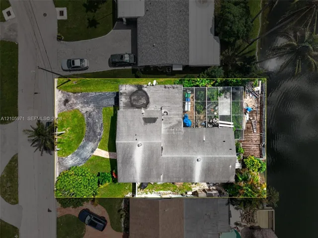 Aerial view of the property featuring a waterfront location, a screened lanai, a paved driveway, and mature landscaping