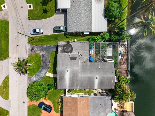 Aerial perspective featuring waterfront property with a screened-in lanai, asphalt driveway, and mature landscaping