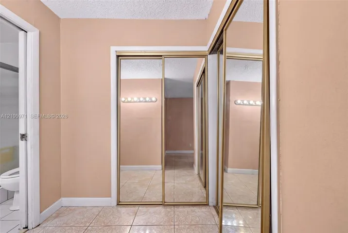 Floor-to-ceiling mirror-paneled sliding closet doors with gold-tone metal framing, ceramic tile flooring, and wall-mounted vanity lighting