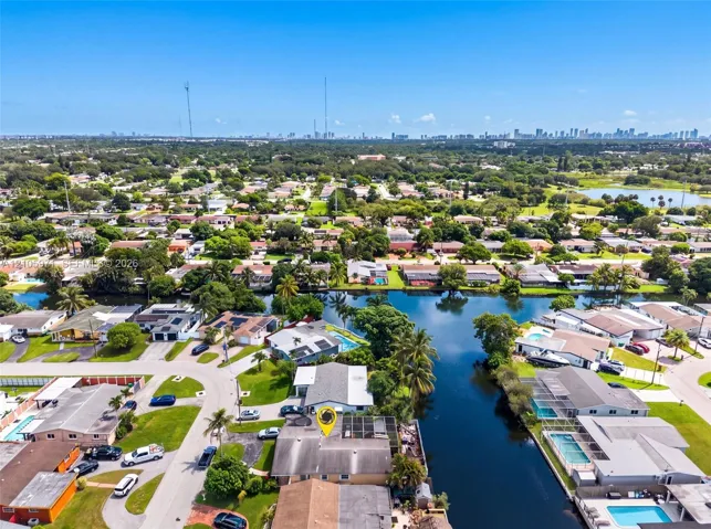 Aerial perspective featuring a waterfront property with direct canal access, mature palm trees, and an expansive skyline backdrop