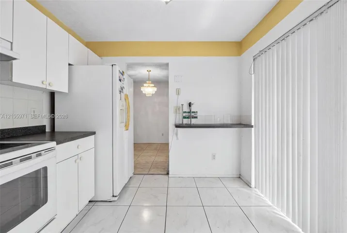 Kitchen featuring white cabinetry, dark countertops, tile flooring, and vertical blinds covering the sliding glass door
