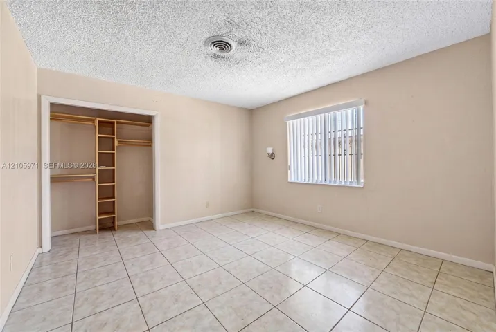 Room featuring tile flooring, a window with vertical blinds, and a built-in closet with integrated shelving