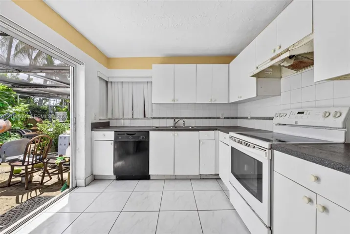 Kitchen featuring white cabinetry, dark countertops, a double-basin stainless steel sink, ceramic tile flooring, and a sliding glass door