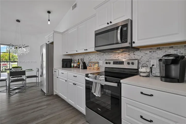 Kitchen featuring white Shaker-style cabinetry, stainless steel appliances, a mosaic tile backsplash, quartz countertops, and wood-finish flooring