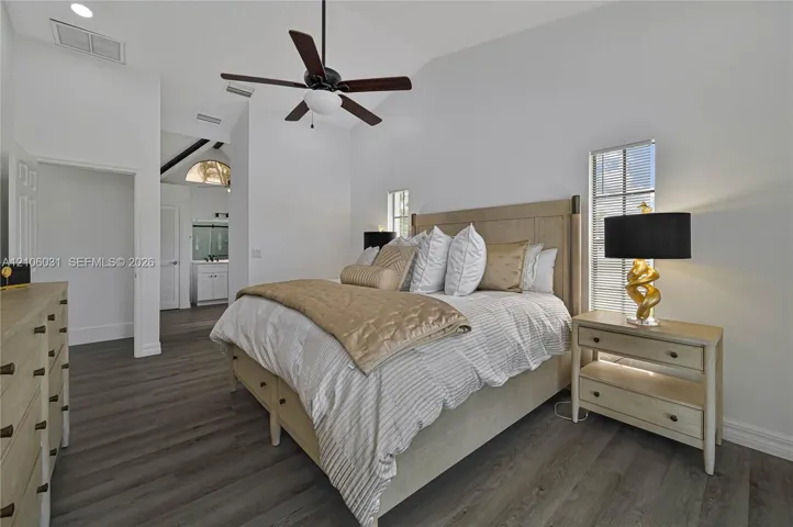 Vaulted ceilings with a central paddle fan, wood-finish flooring, and tall windows