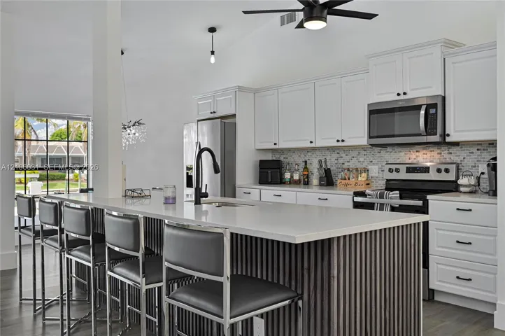 Kitchen featuring white shaker-style cabinetry, quartz countertops, a slatted wood-finish kitchen island, a mosaic tile backsplash, and stainless steel appliances