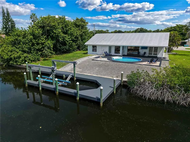 Waterfront property featuring a private boat dock with a mechanical lift, an in-ground swimming pool, a metal roof, and stone-surfaced patio area