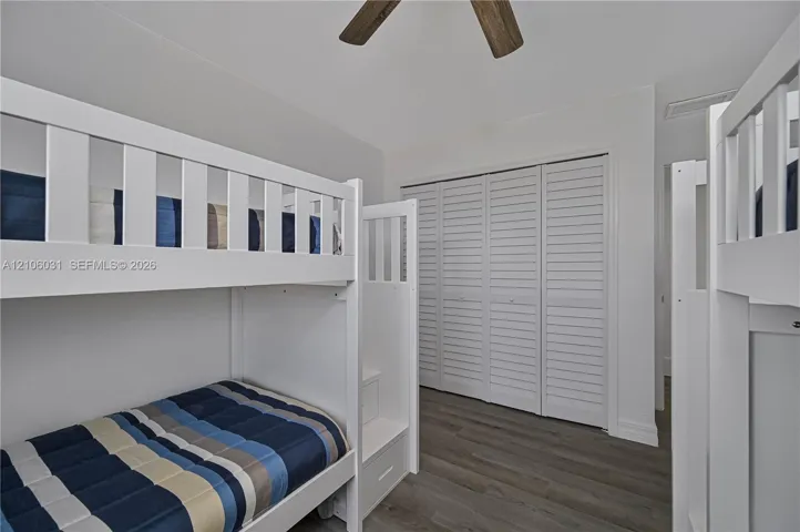 Wood-finish flooring, white louvered closet doors, and a ceiling fan