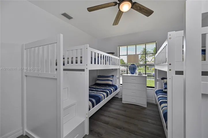 Room featuring wood-finish flooring, a multi-blade ceiling fan with integrated lighting, and a window with exterior water and landscape surroundings