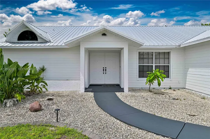 Exterior facade featuring white horizontal siding, a metal roof, a semi-circular accent window, and double entry doors