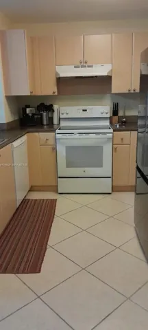 Kitchen featuring light-finish cabinetry, neutral solid-surface countertops, white electric range with overhead ventilation, and diagonal-set floor tile