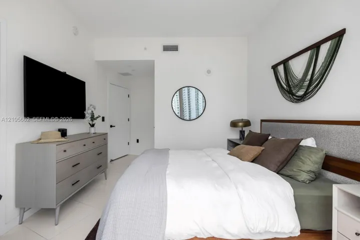 Neutral-toned room featuring large-format tile flooring, smooth white wall finishes, and a circular wall-mounted mirror