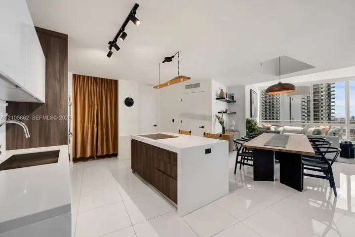 Kitchen featuring a central island with a solid-surface countertop and wood-finish cabinetry, gloss-finish white upper cabinets, track lighting, built-in shelving, and floor-to-ceiling windows