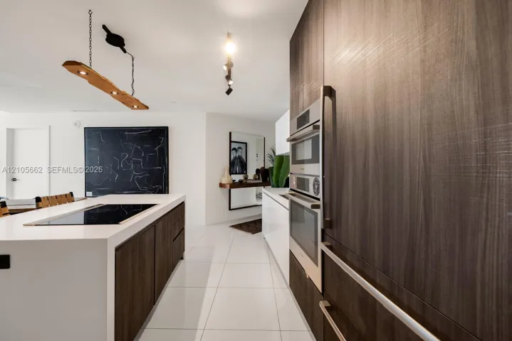 Kitchen featuring full-height wood-finish cabinetry, built-in double wall ovens, a large island with a surface-integrated cooktop, and large-format porcelain tile flooring