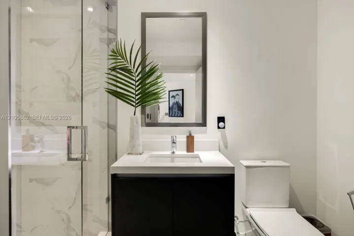 Modern vanity with a countertop basin and cabinet storage, framed wall mirror, glass-enclosed shower with large-format tile surround, and dual-flush toilet
