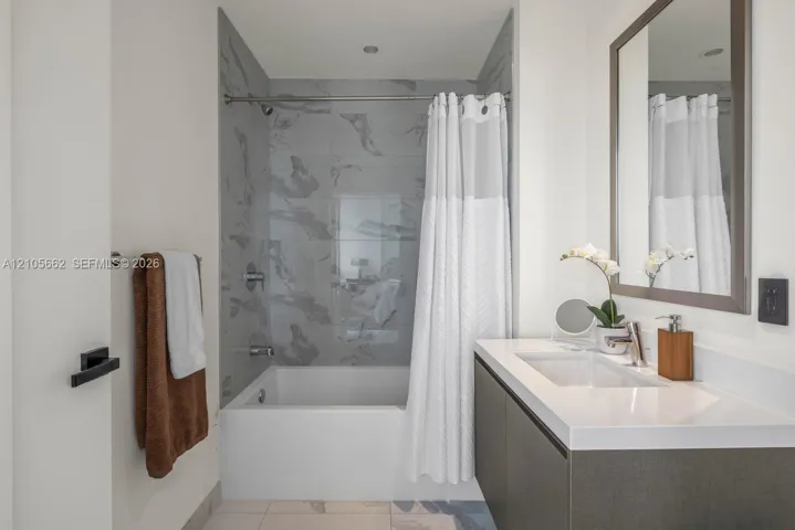 Wall-mounted floating vanity with integrated rectangular sink and solid surface countertop, mirror with framed border, and bathtub featuring patterned wall tile