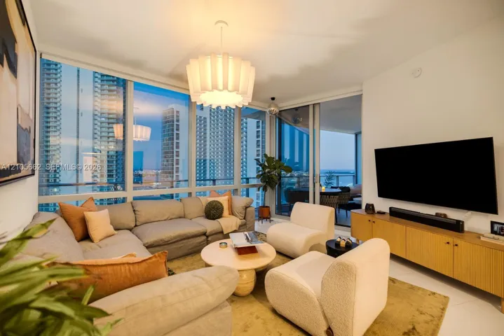Living area featuring floor-to-ceiling windows, white tile flooring, custom drum pendant lighting, and a sliding glass door providing external access